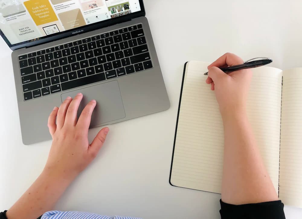 A person taking notes beside a laptop